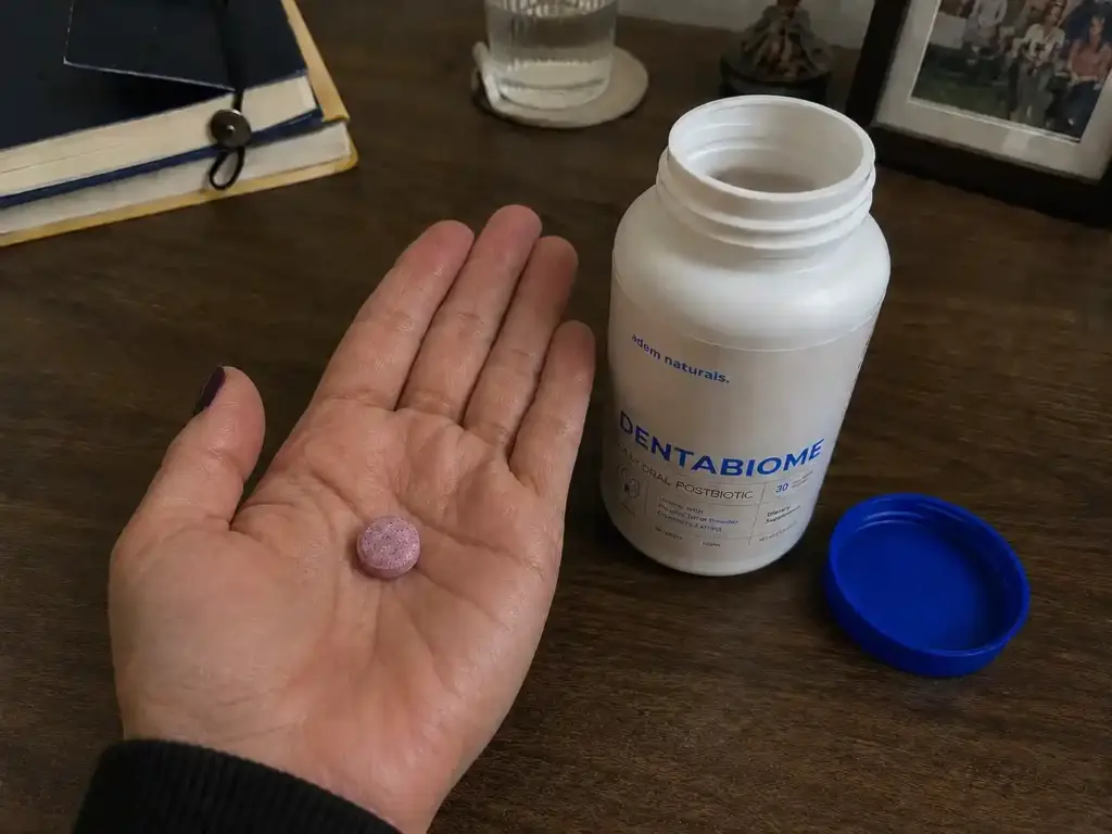 DentaBiome chewable tablet displayed in hand beside an open DentaBiome supplement bottle