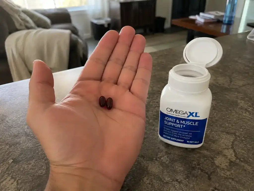 Hand holding Omega XL softgels beside open bottle